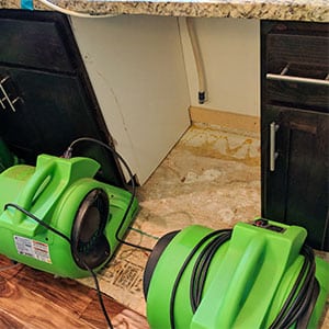 Water damage restoration in progress showing commercial dryers drying out a leaky dishwasher area in a kitchen due to water damage